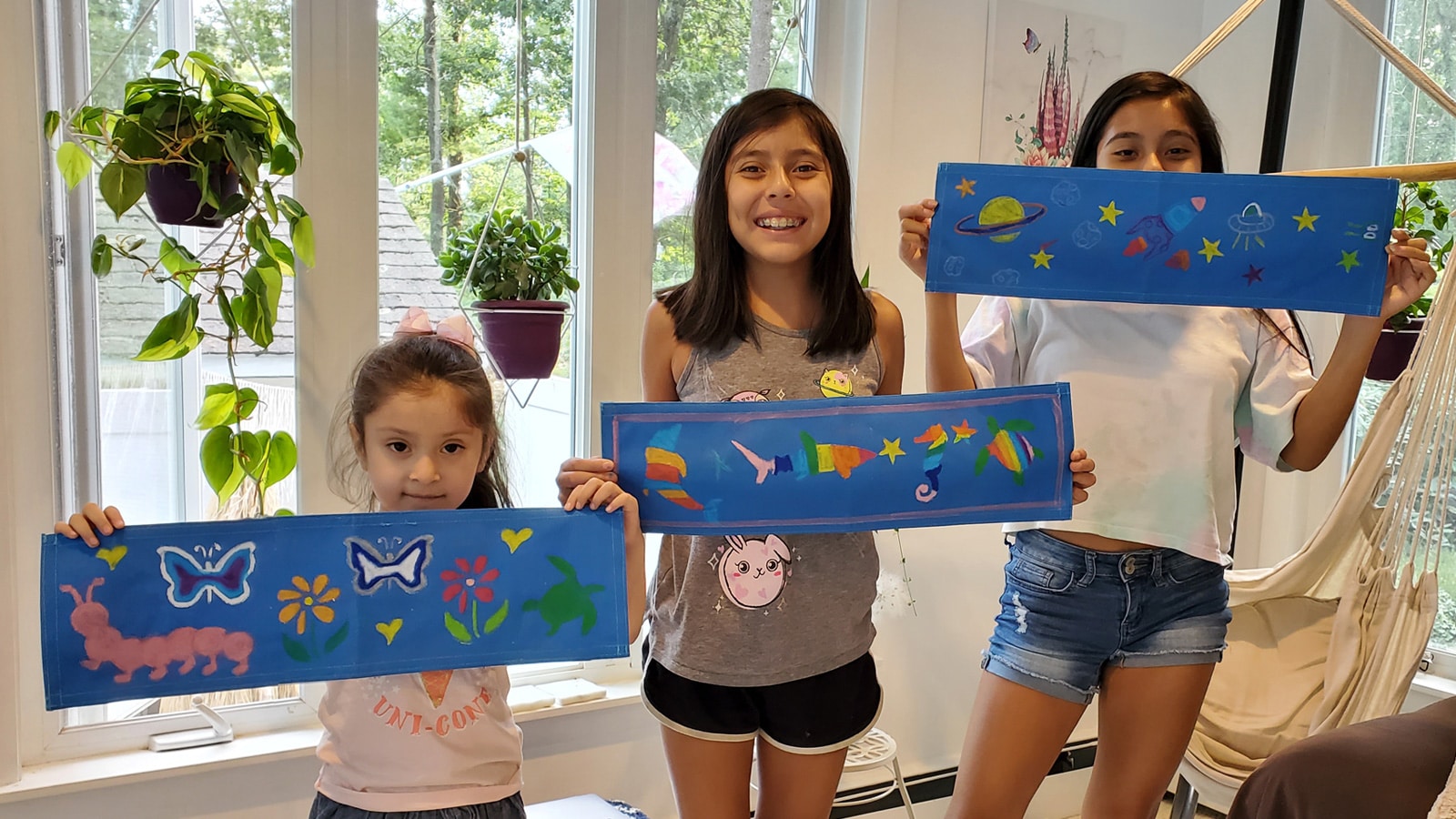 Three young girls smiling to camera and showing off their artwork 