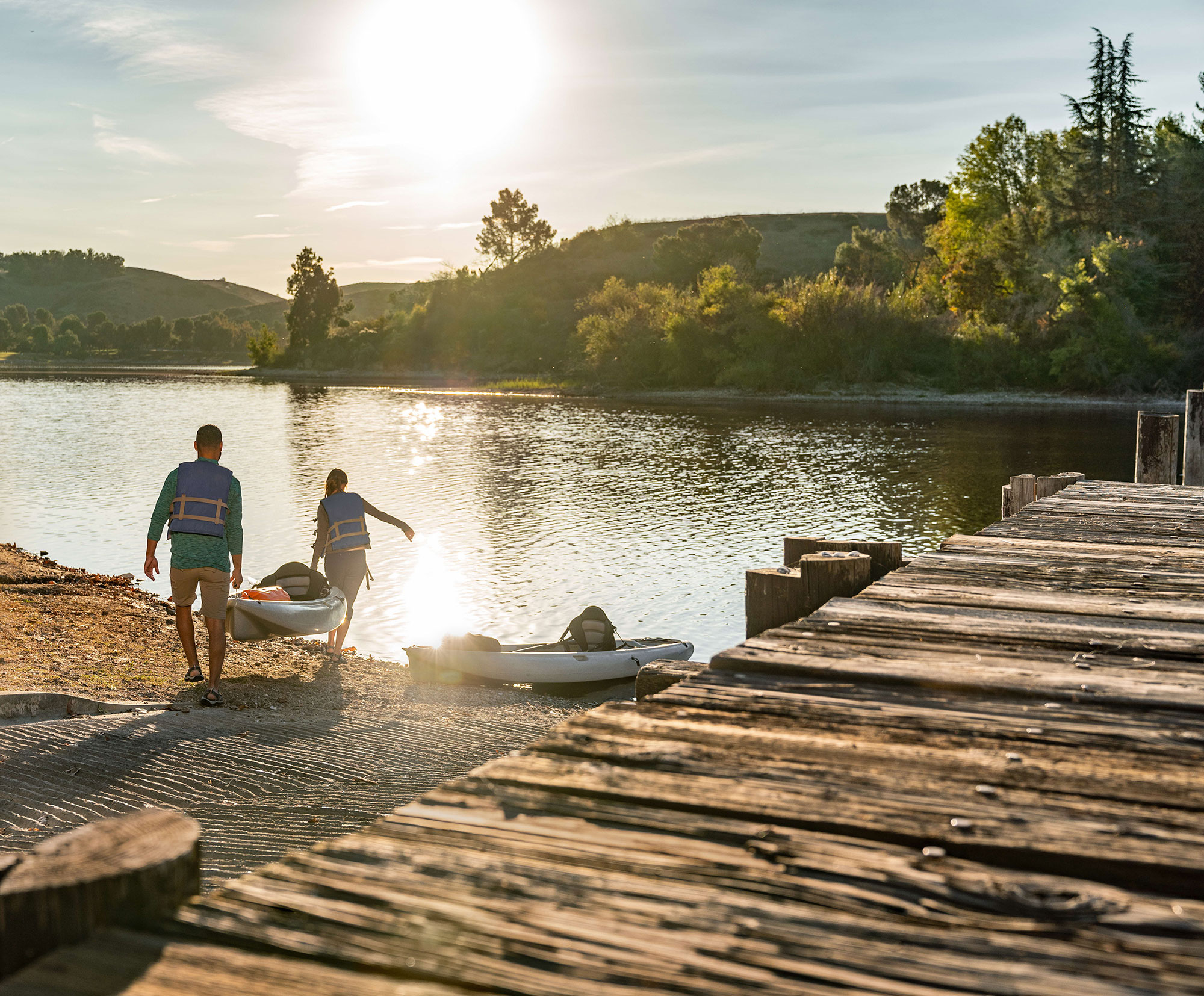 Two people carrying a kayak to water, facing away from the camera