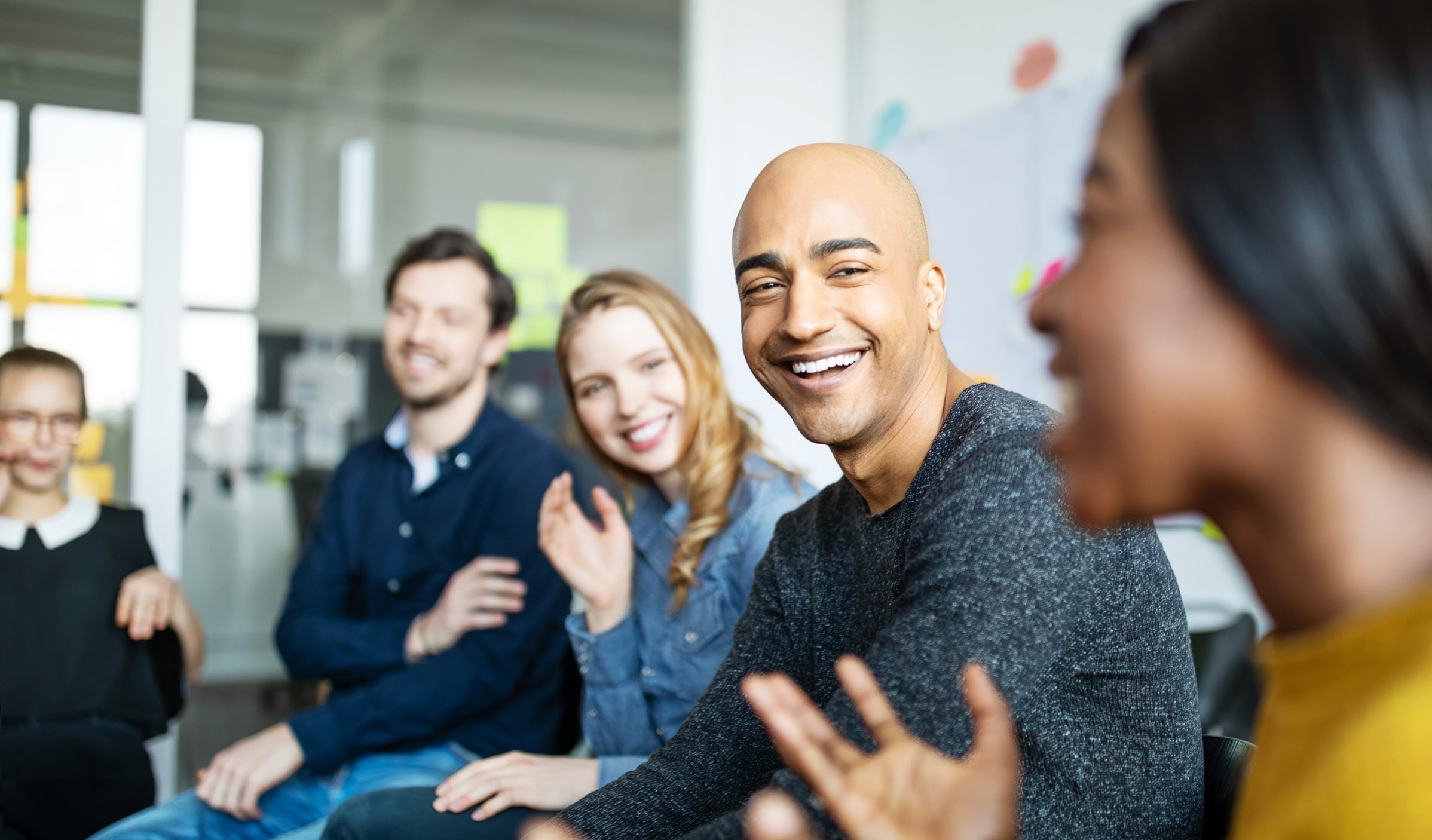 Group of men and women of all ethnicities, sitting in an office setting laughing and conversing