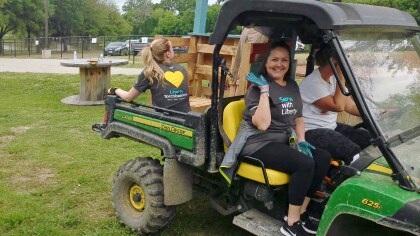 LM employee participating in Serve with Liberty, riding in a lawnmower smiling to camera