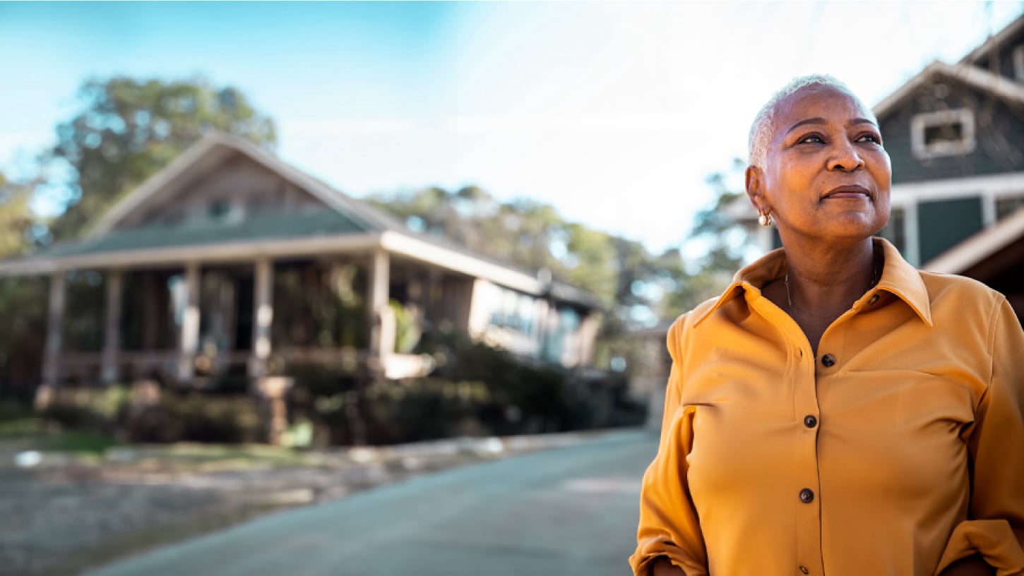 A woman outside, with houses in the background, looking off camera