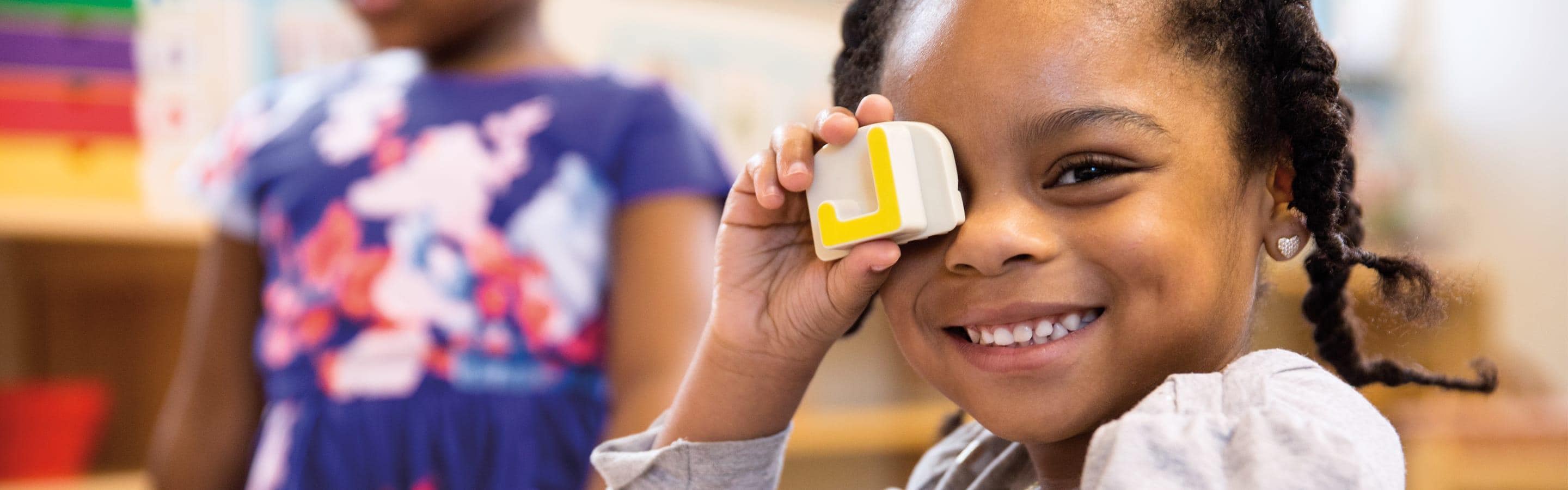 Young girl smiling holding a block up to her eye