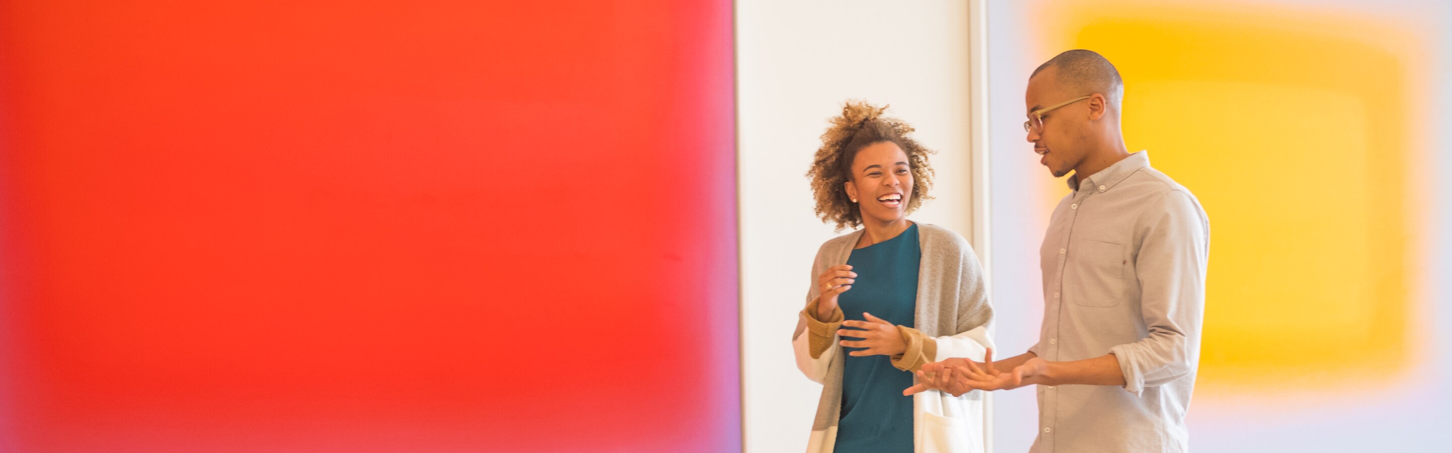 Two employees, walking and talking in an office hallway, with two large paintings on the wall