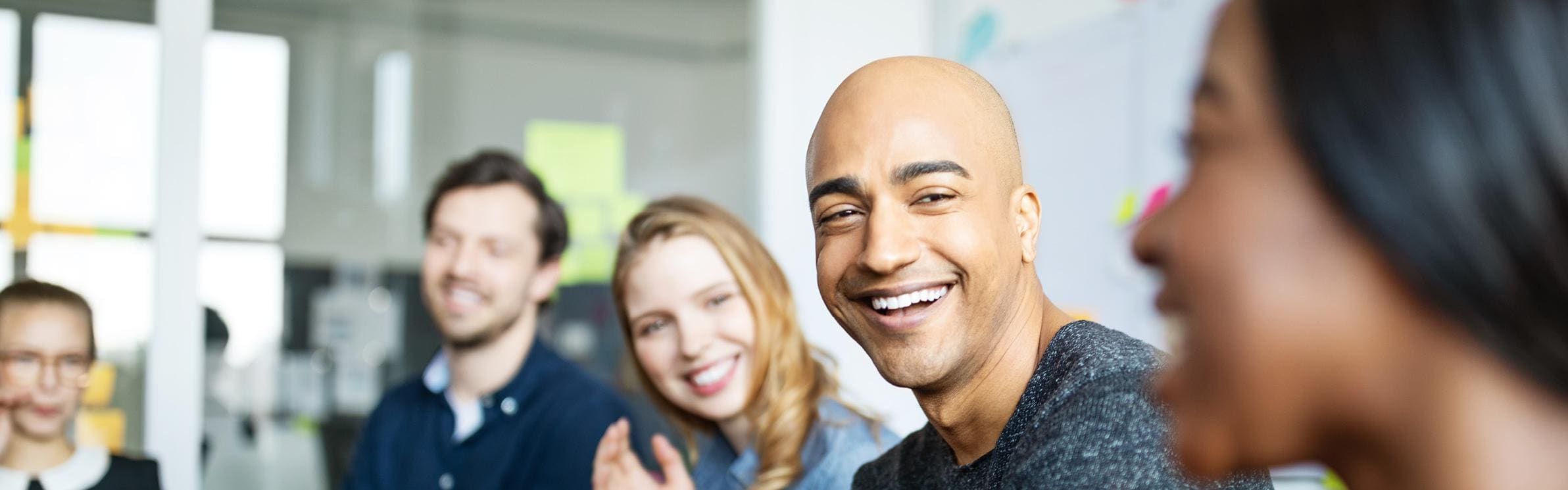 Group of men and women of all ethnicities, sitting in an office setting laughing and conversing