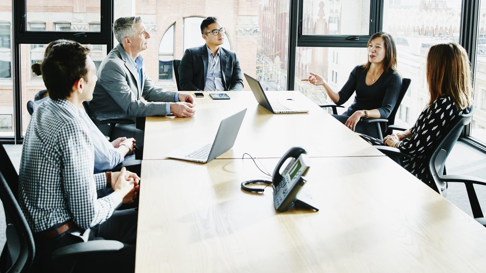 Men and Women discussing topics while sitting at a table in a conference room 