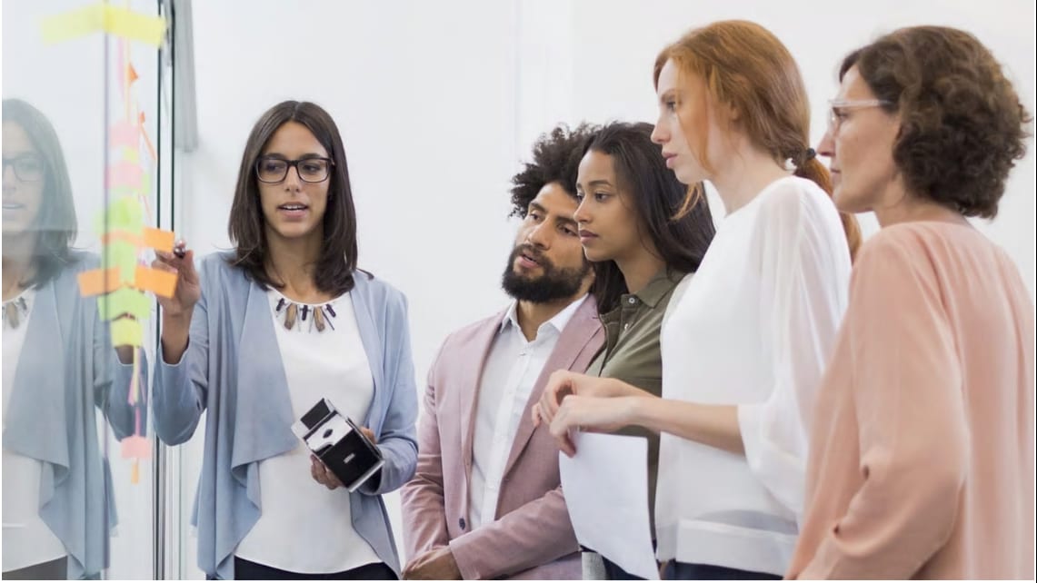 five employees gathered around a whiteboard talking