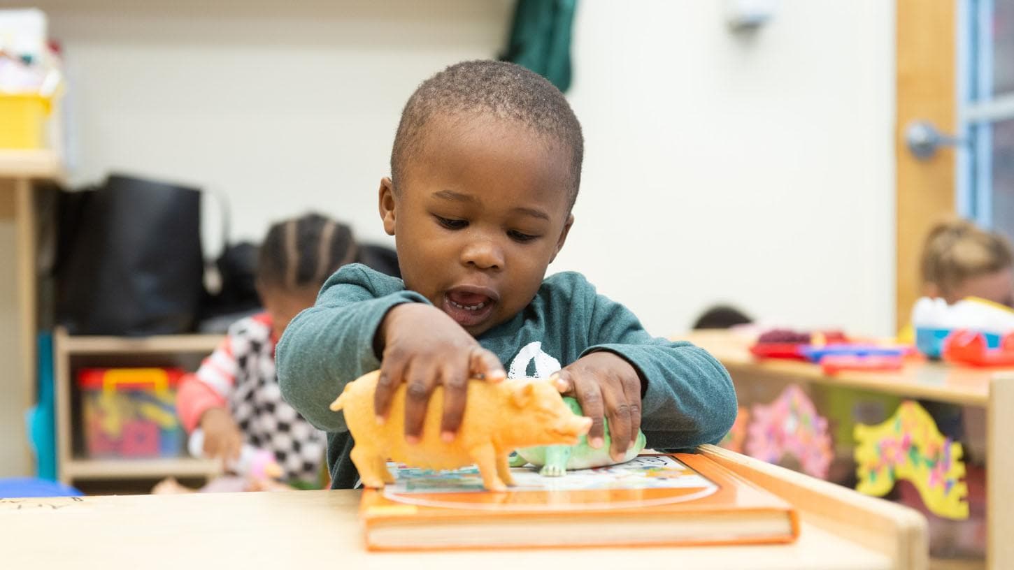 (slide 3 of 7) Toddler playing with plastic big toy in classroom. 