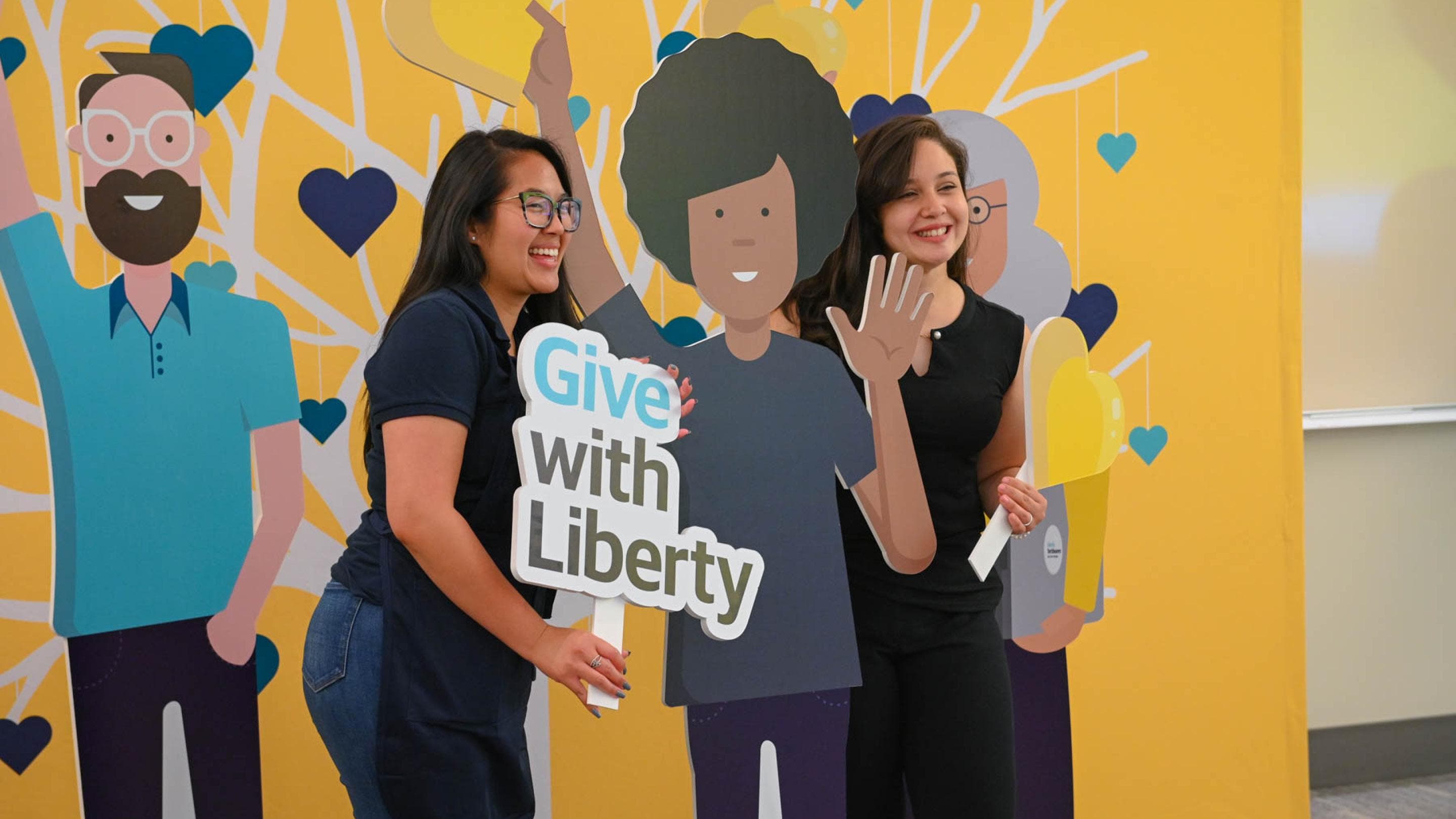 (slide 1 of 5) Two Liberty Mutual employees posing with a Give with Liberty sign. 
