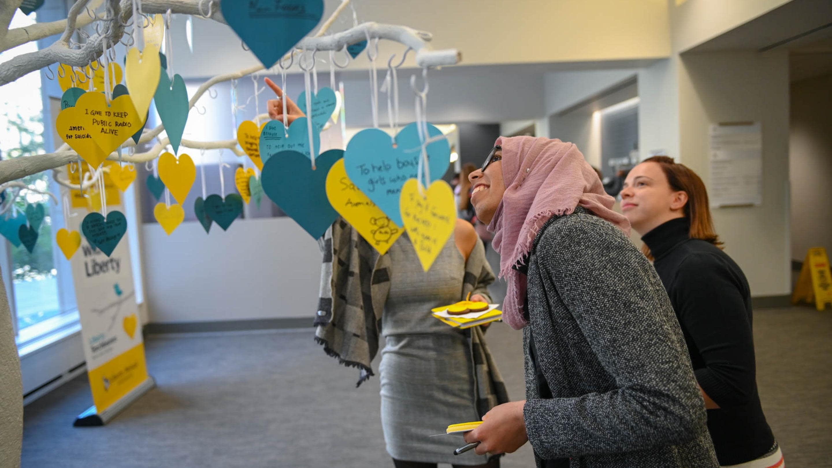 (slide 4 of 5) Group of women looking at the Give with Liberty donation tree. 