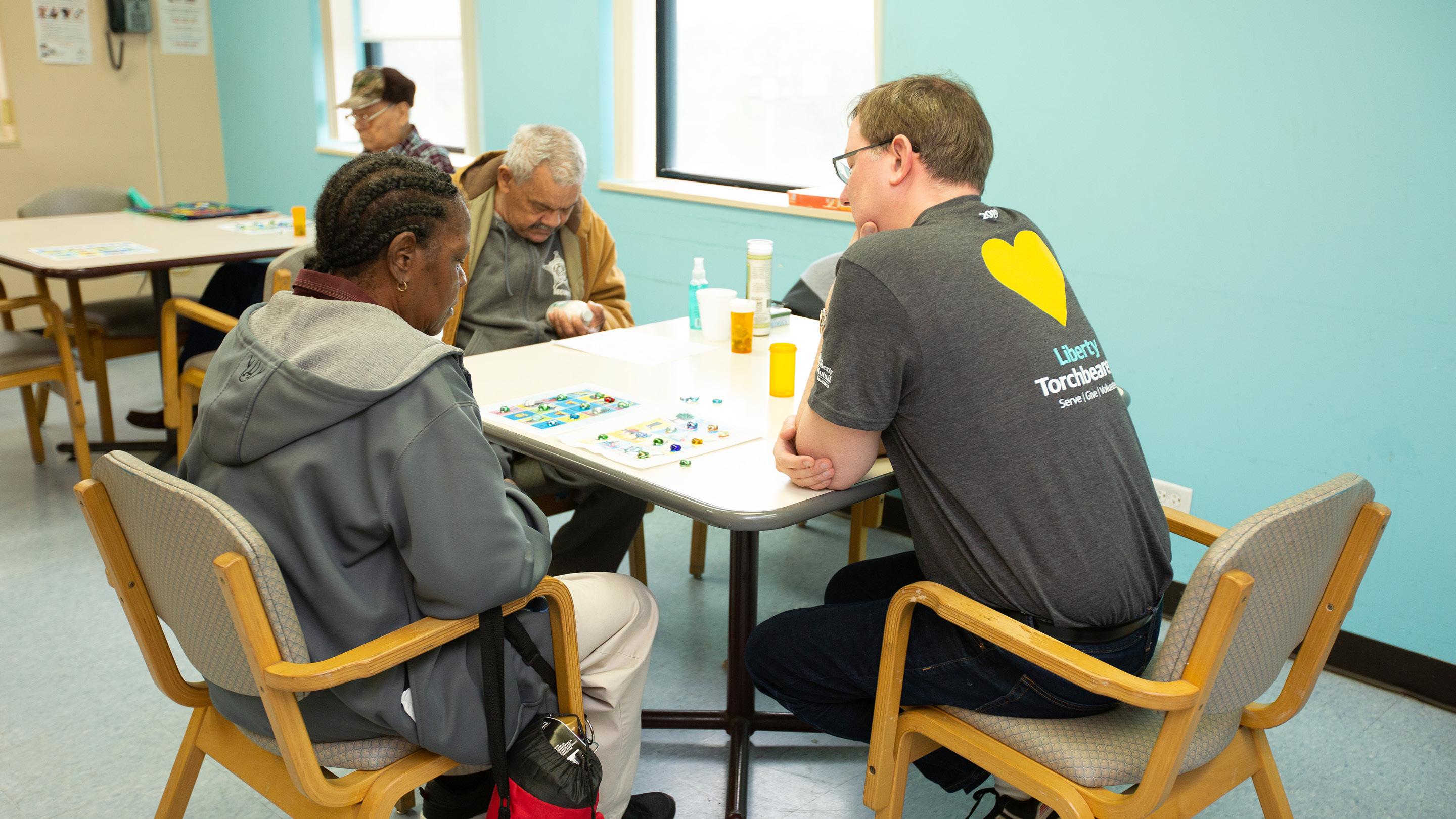 (slide 4 of 6) Men at a desk reading and laying games. 