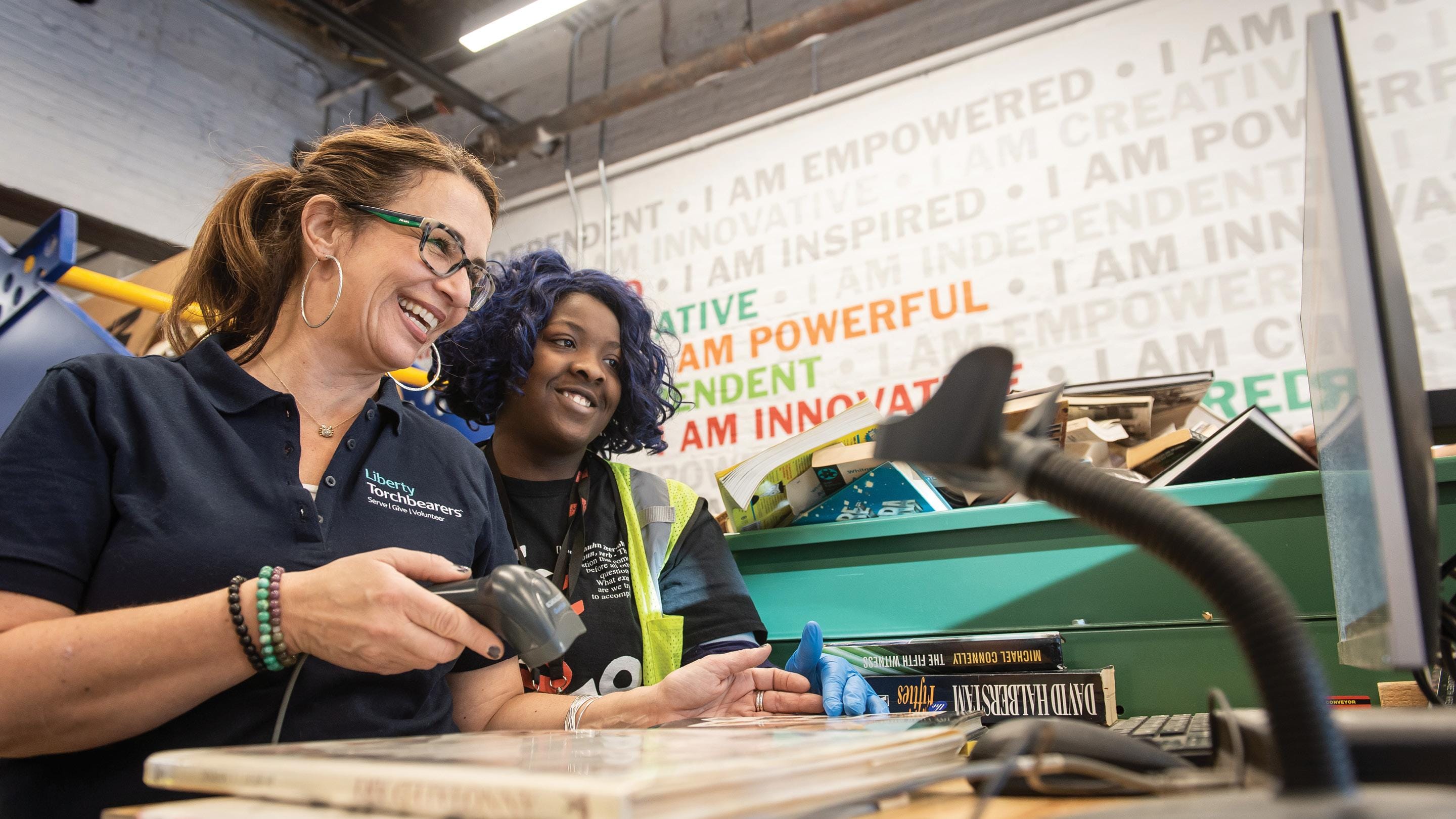 (slide 3 of 4) Two women smiling, ringing up books at a cash register. 