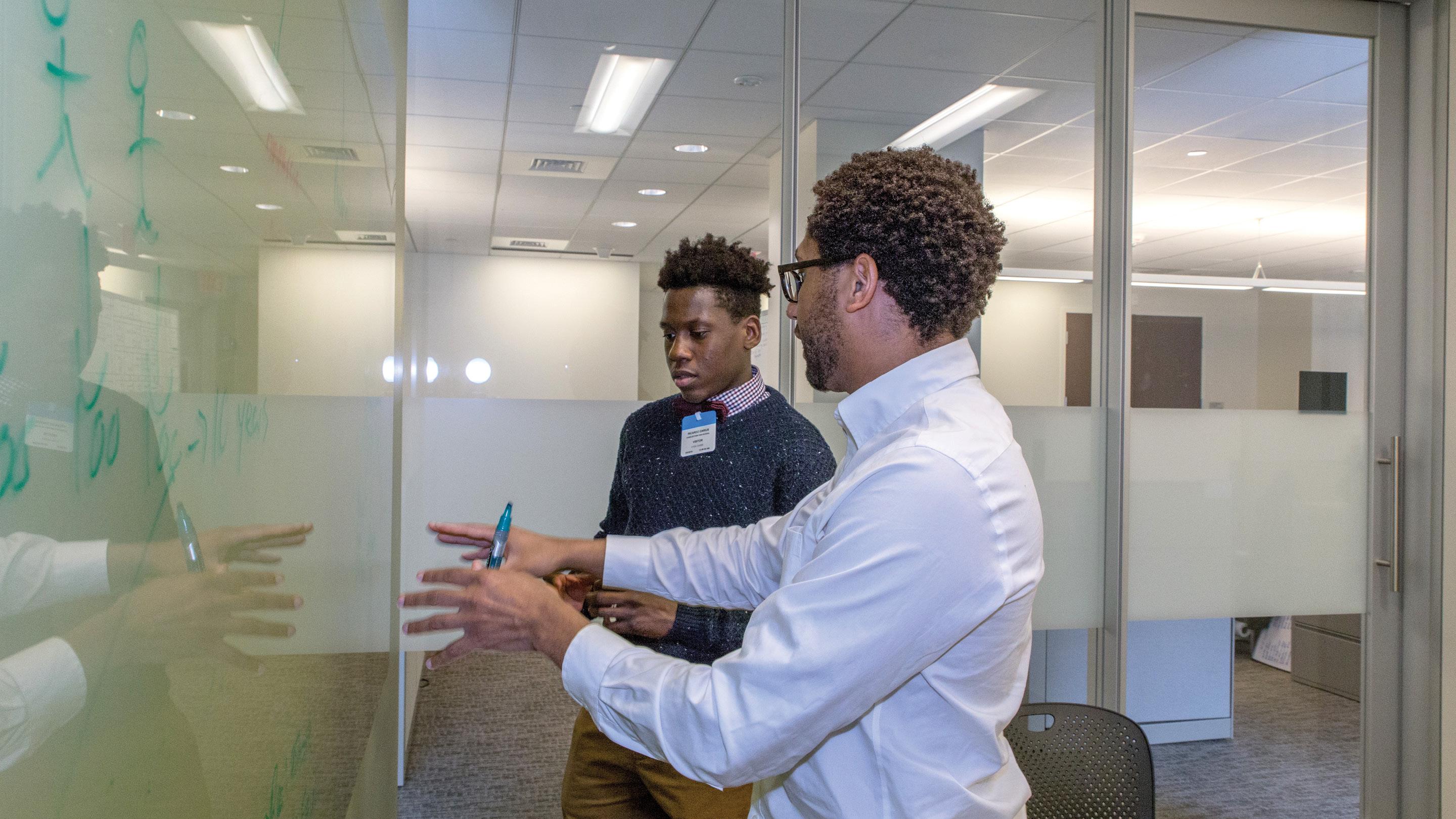 (slide 4 of 4) Two men talking in front of a white board during a brainstorming session. 