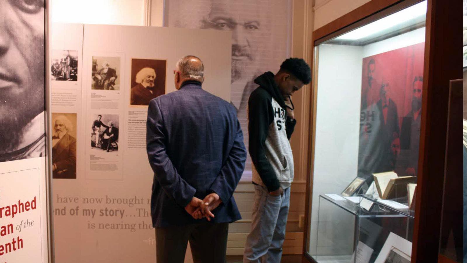 Two black men, one a teen and one an older gentlemen, lookin gat Frederik Douglas exhibits at The Museum of African American History