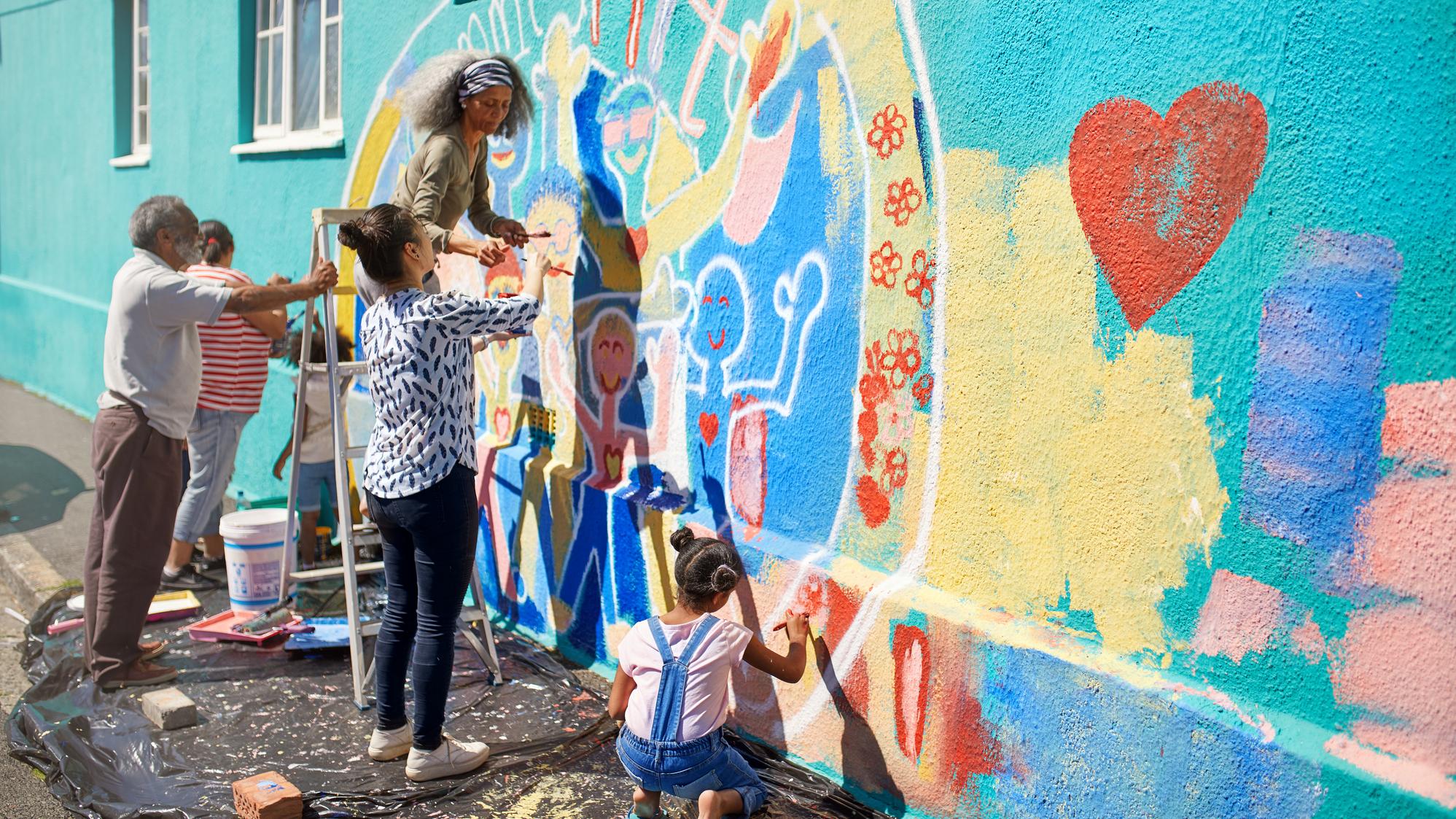 Group of people painting an exterior wall with a colorful mural 