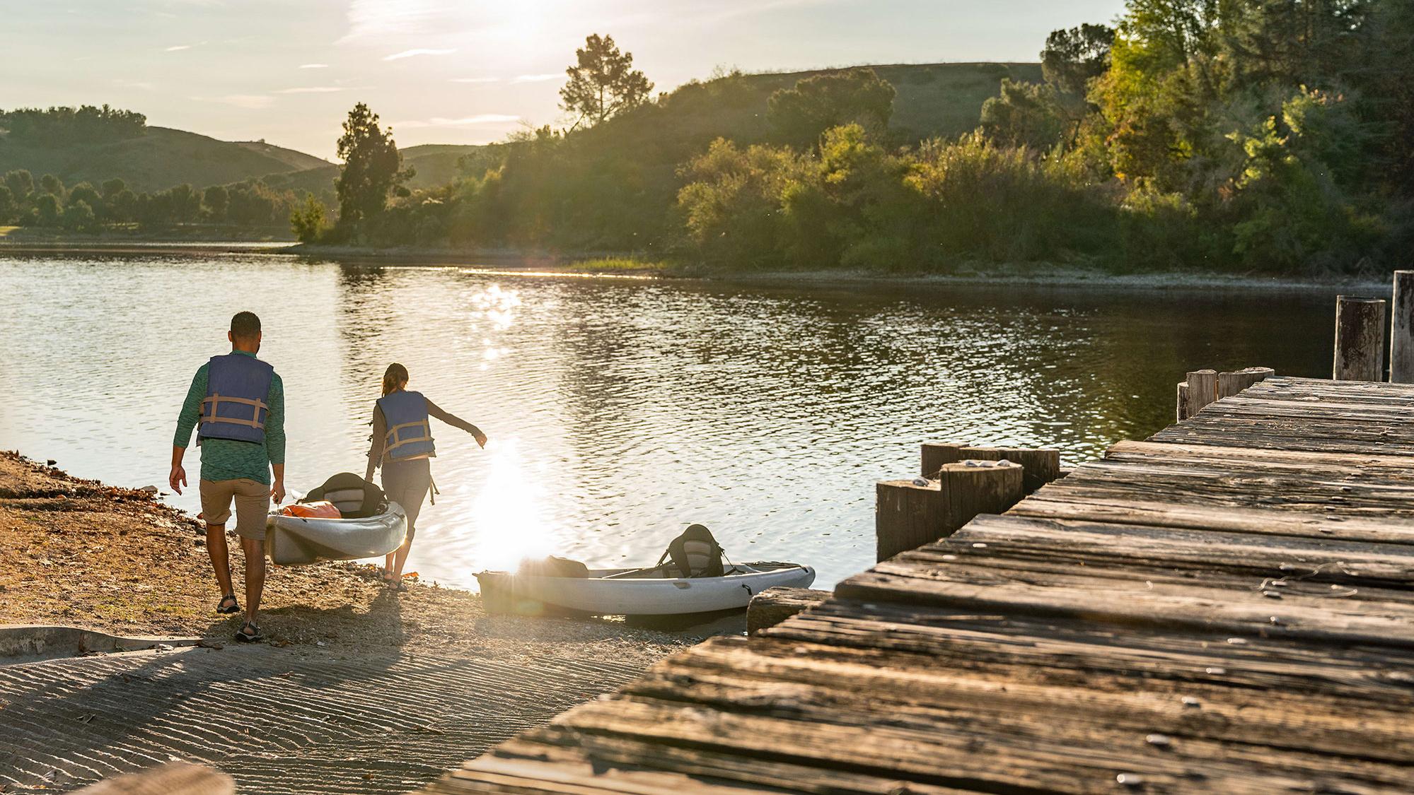 Two people carrying a kayak to water, facing away from the camera