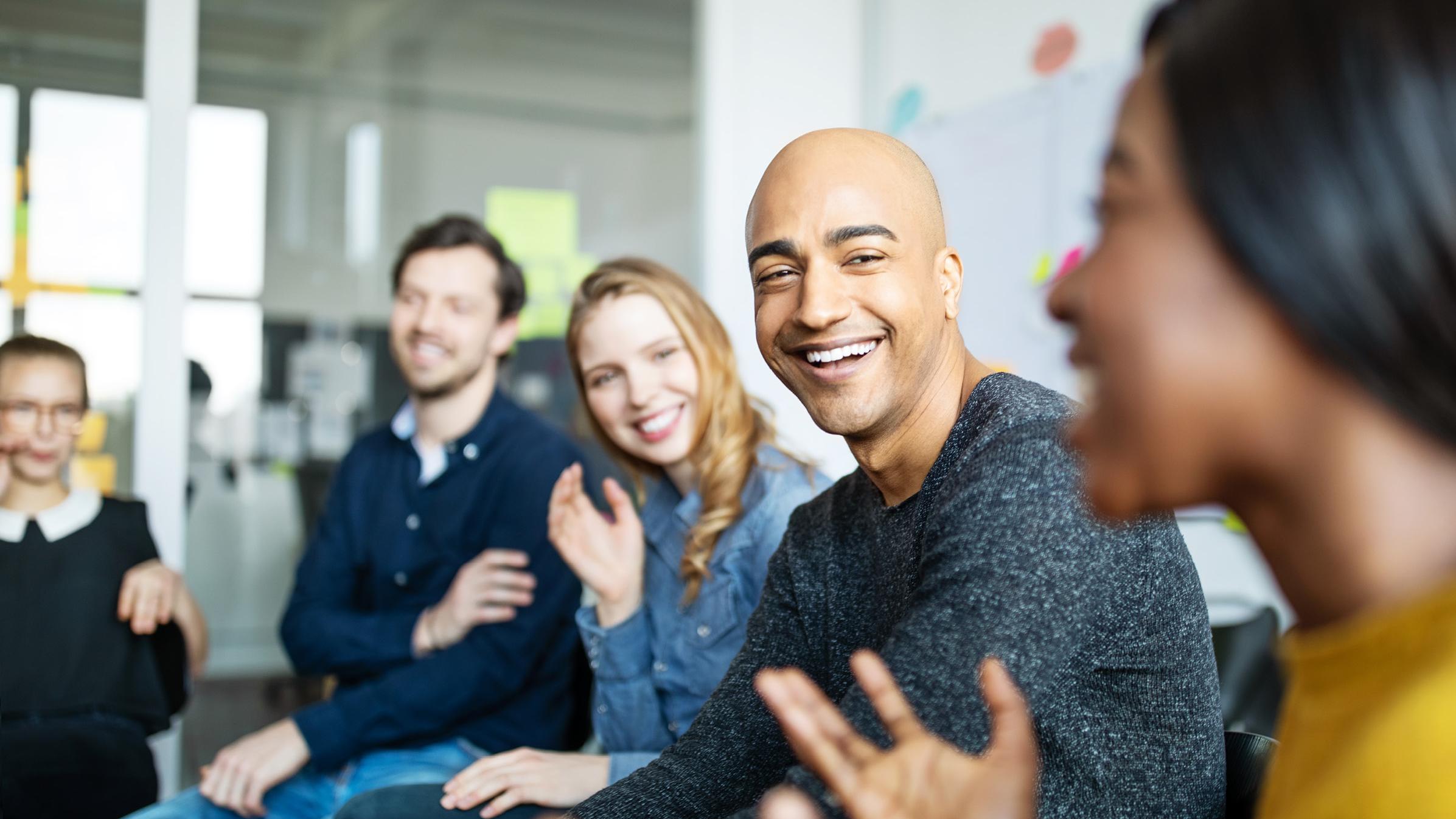Group of men and women of all ethnicities, sitting in an office setting laughing and conversing