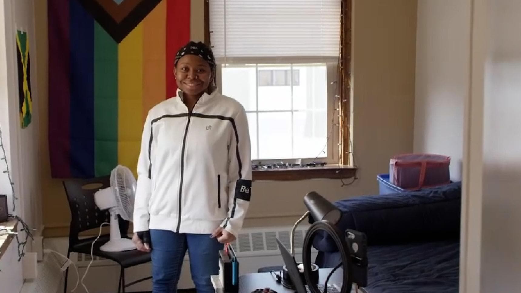 Young person standing in a dorm like room, smiling to camera 