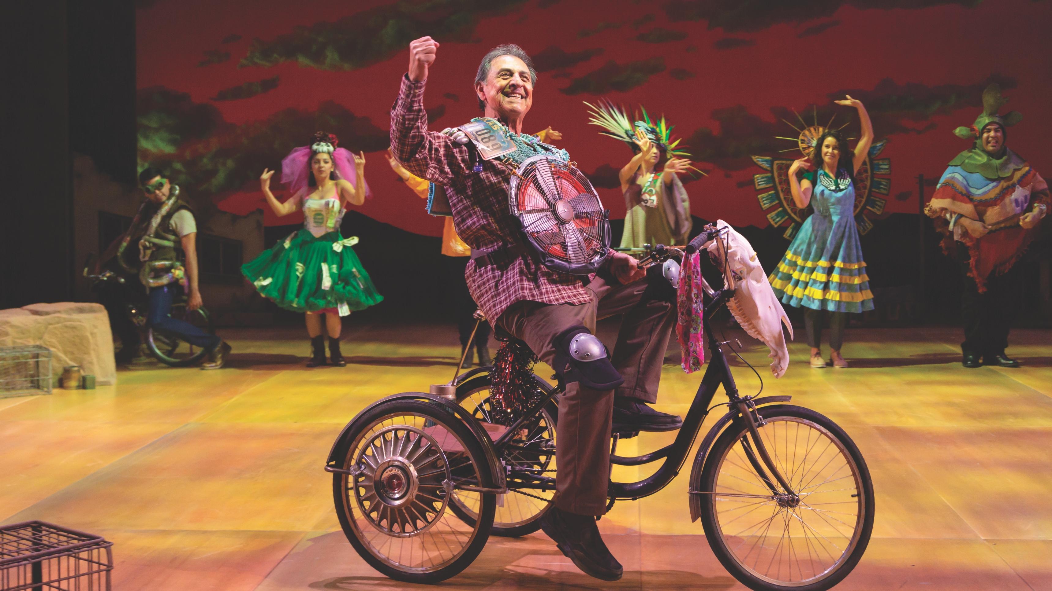 A man in costume riding a bike on stage indoors