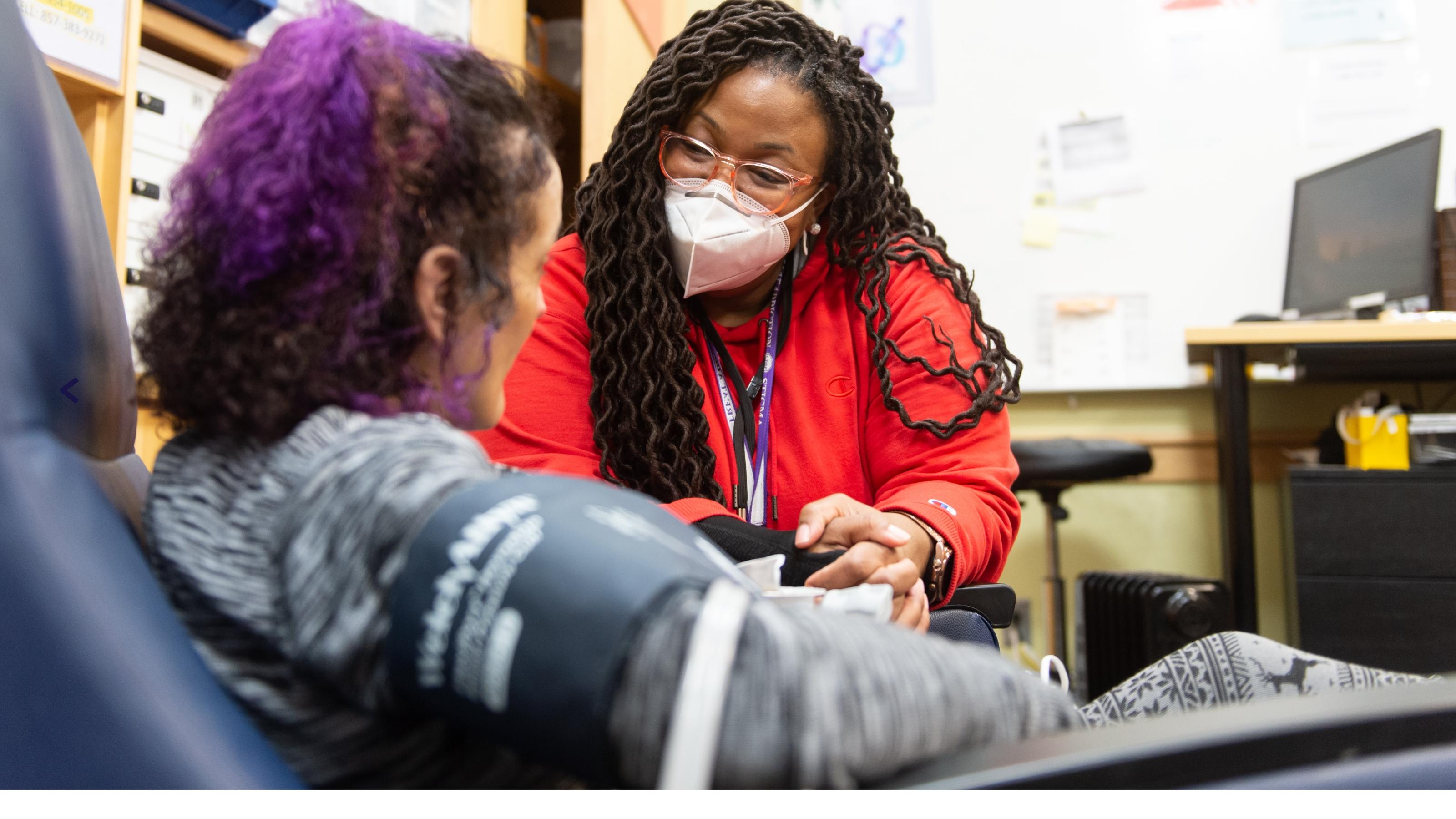 (slide 4 of 6) A masked woman taking the blood pressure of a young woman . 