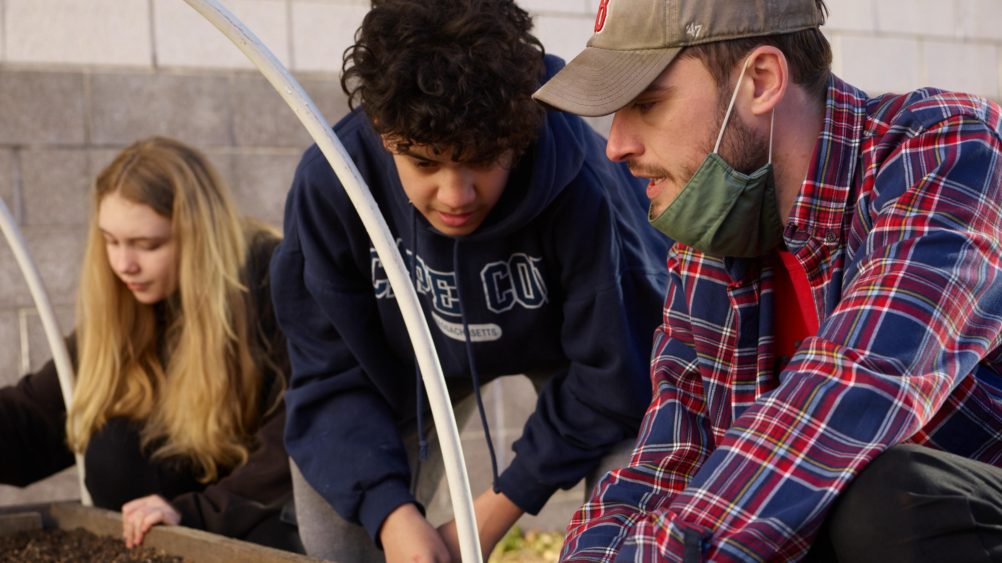 (slide 3 of 4) Three young people outdoors planting a garden. 