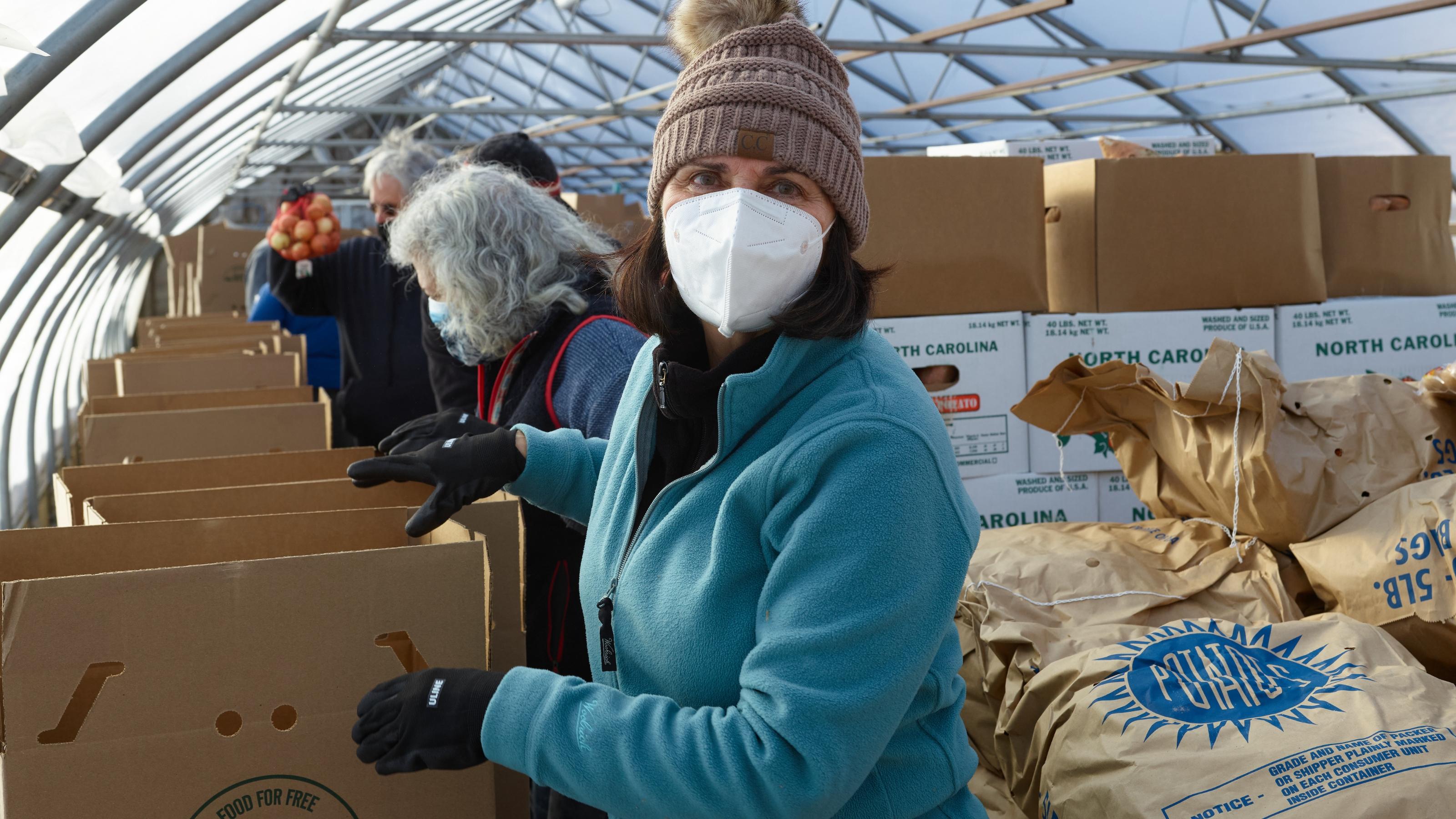 (slide 5 of 6) A masked woman packing food at Boston Area Gleaners . 