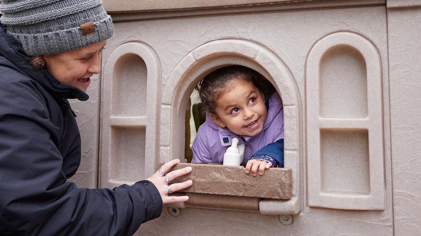A child and adult playing outside in a playhouse