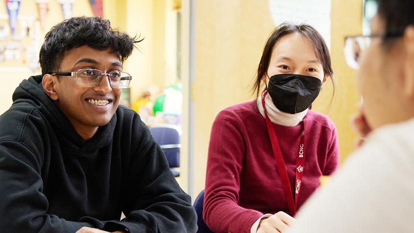 Two teens one masked, working and smiling to camera