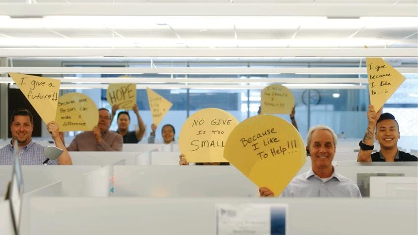 Liberty Mutual employees holding up yellow shapes with words about why the Give 