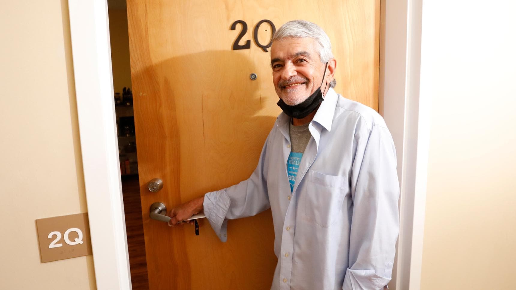 A man smiling to camera, opening the door to his room at Pine Street