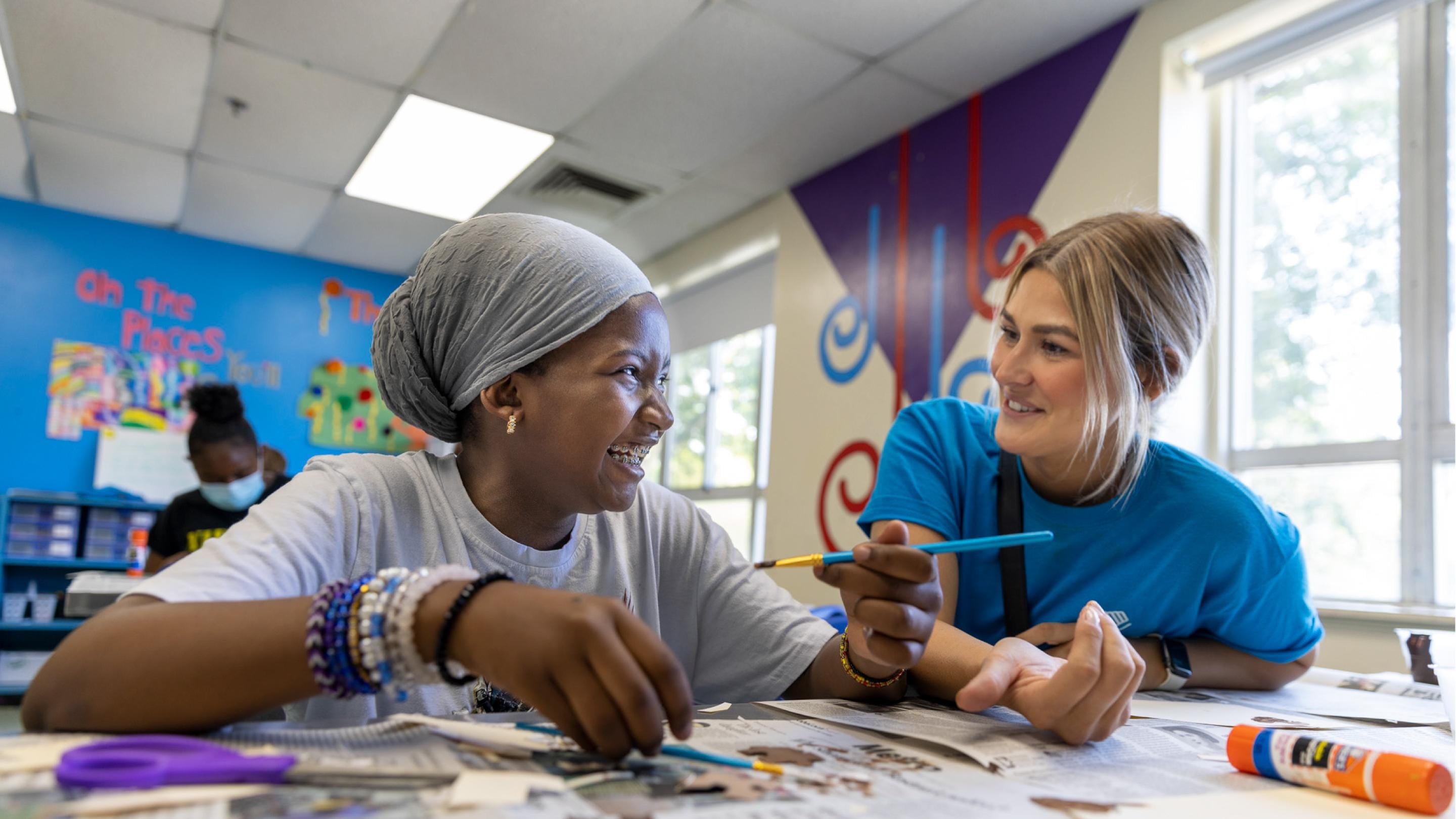 (slide 2 of 5) A volunteers doing crafts with a student at the centers. 