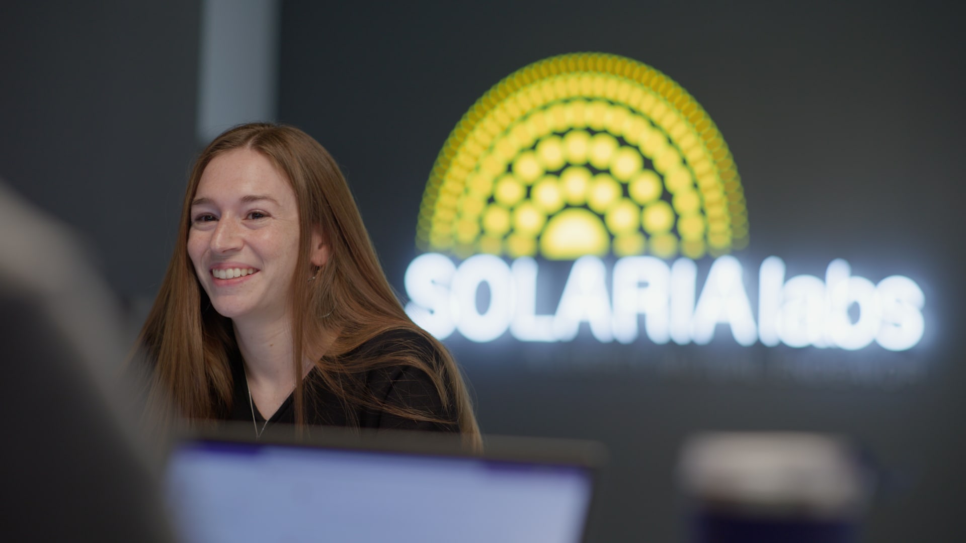 Woman sitting in front of a glowing Solaria Labs sign