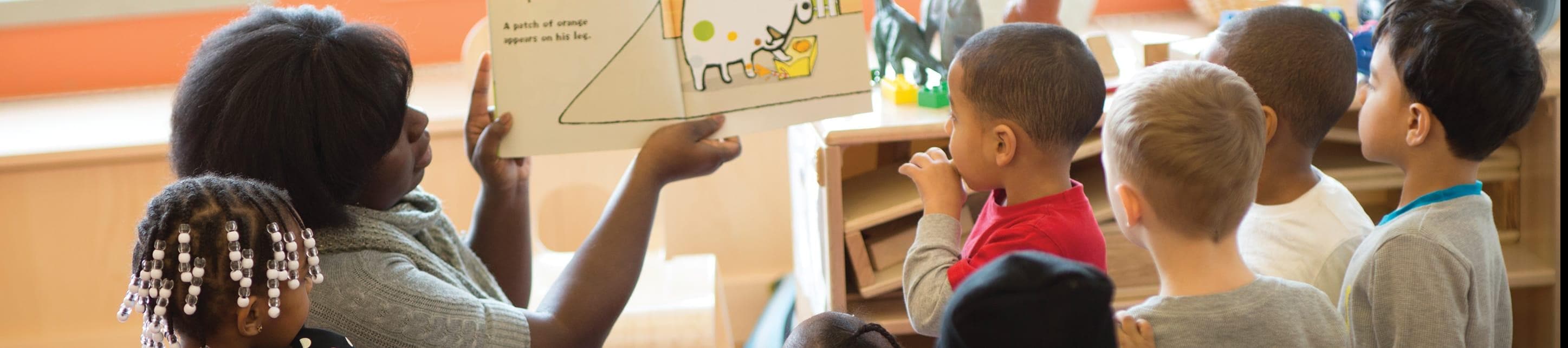 A teacher reading a book to about six young kids in a classroom