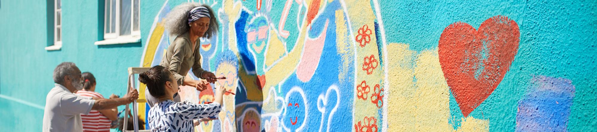 Group of people painting an exterior wall with a colorful mural