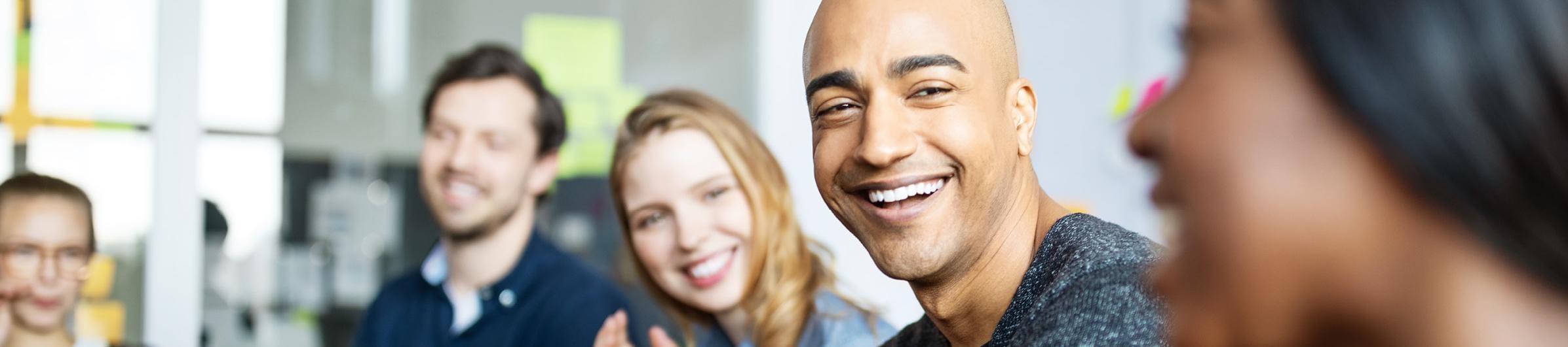 Group of men and women of all ethnicities, sitting in an office setting laughing and conversing