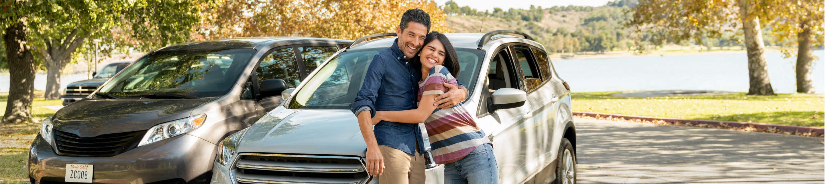 Two people embracing outside in front of a car