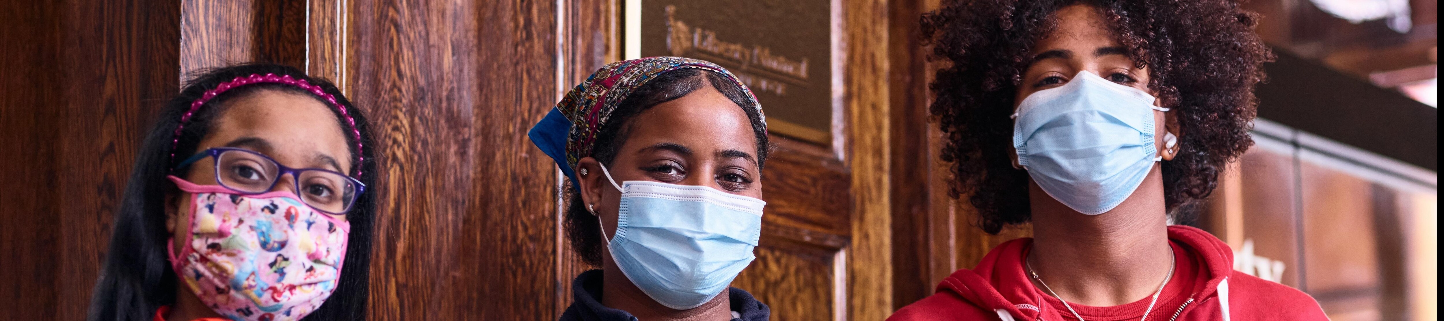 Three young people wearing face masks and smiling to camera
