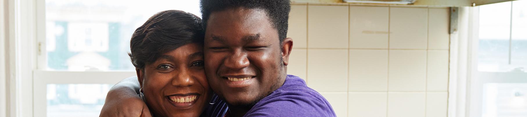 A woman and teen embracing and smiling to camera