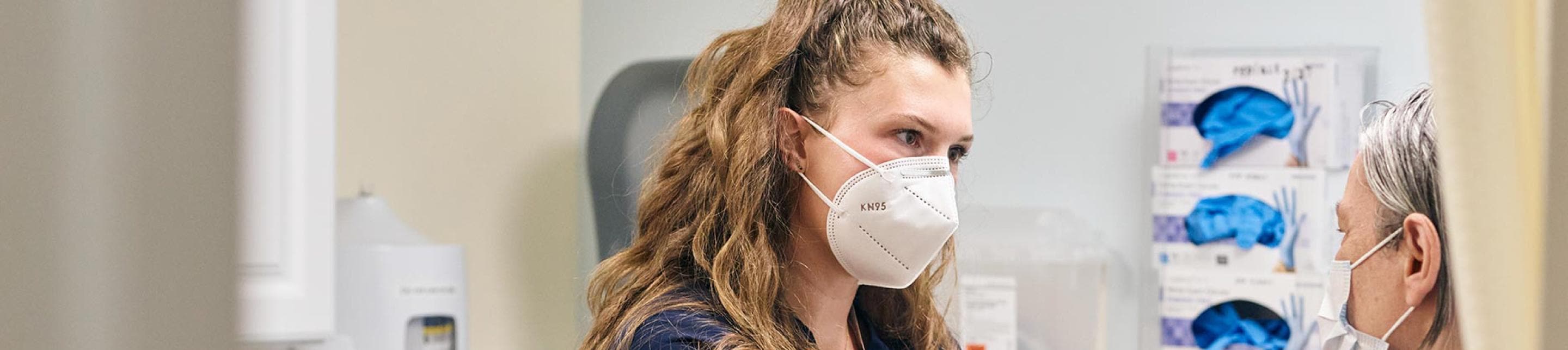 A medical professional in a mask, speaking to a patient