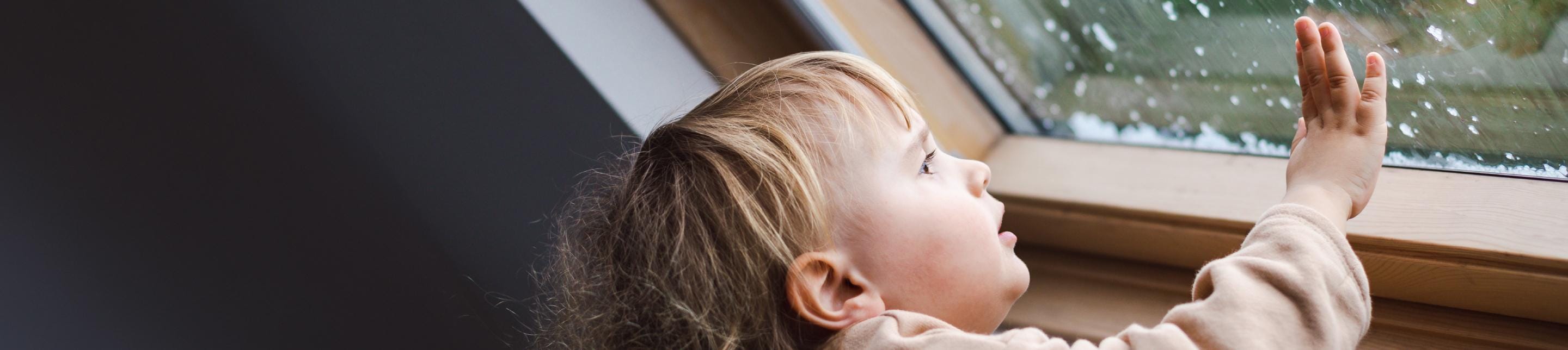 A young child staring out a rainy window and touching the glass