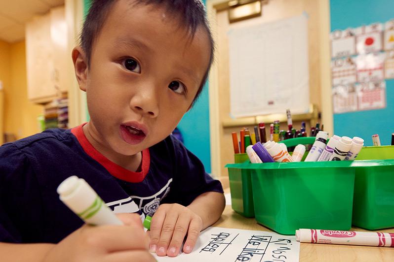 Child coloring with markers at desk in school